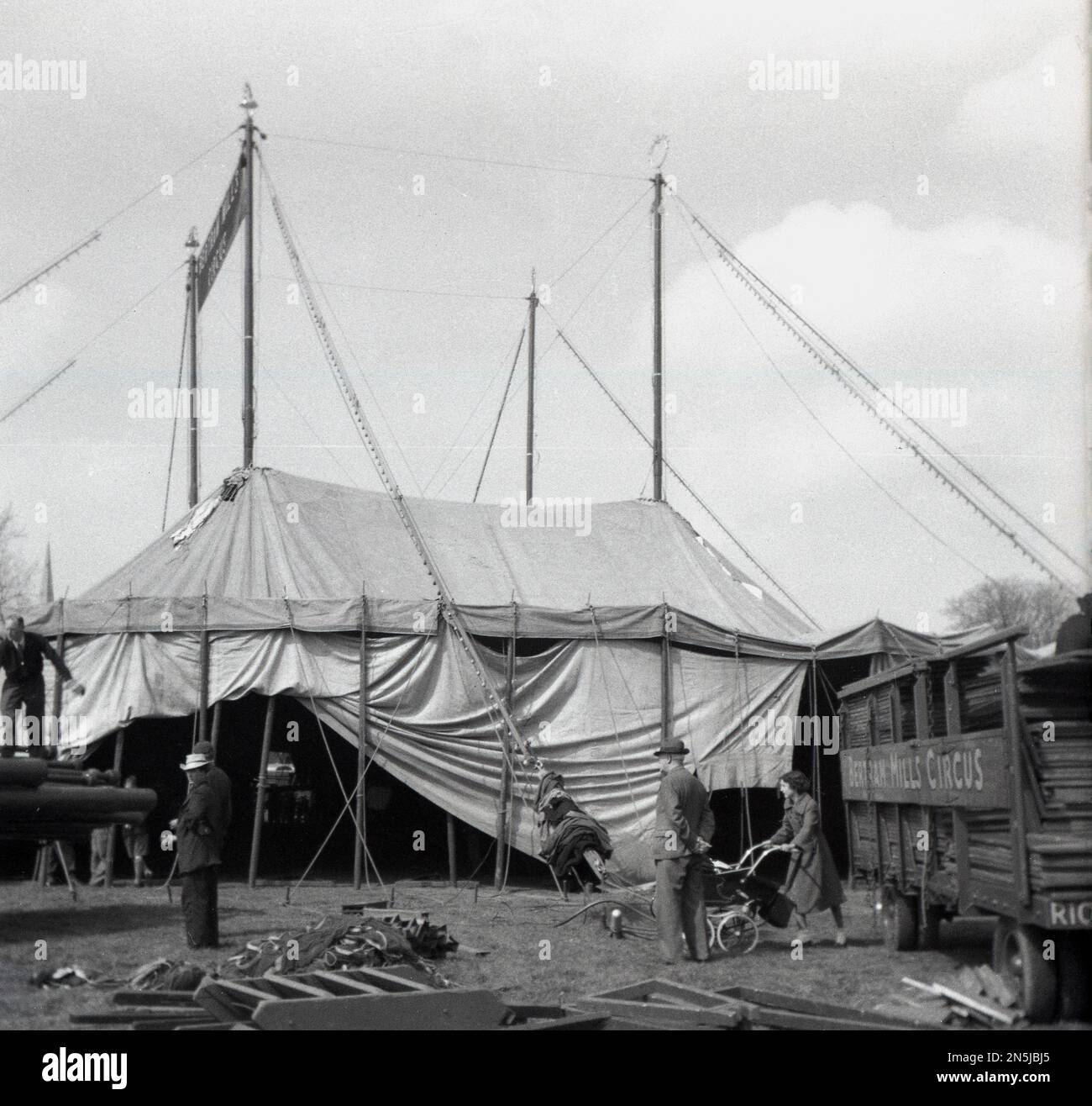 1955, historisch, kommt der Zirkus in die Stadt und baut das große Zelt des Bertram Mills Zirkus, Cambridge, England, Großbritannien, eine Mutter mit einem Kinderwagen, die an einem Lastwagen und Zirkusarbeitern vorbeiläuft. Stockfoto