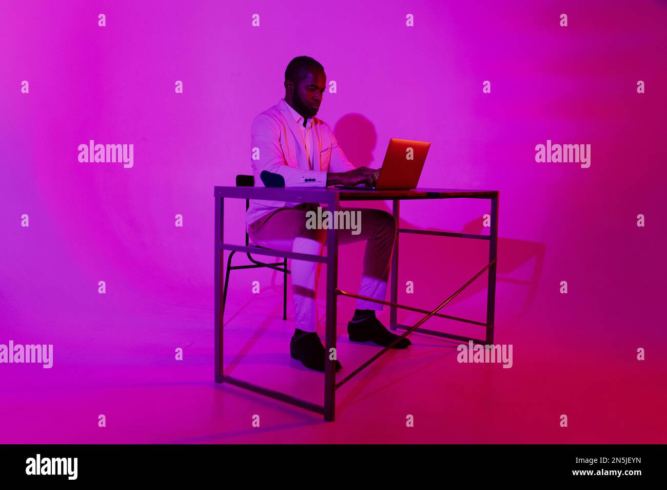 Ein Mann sitzt am Schreibtisch. Ein schwarzer Programmierer arbeitet mit einem Laptop. Der Mann arbeitet nachts. Stockfoto