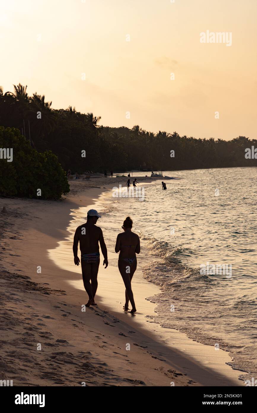 Maldives Beach - ein Paar auf einem Langstreckenurlaub am Ufer bei Sonnenuntergang an einem Sandstrand, Rasdhoo Atoll, die Malediven, Indischer Ozean Asien Stockfoto