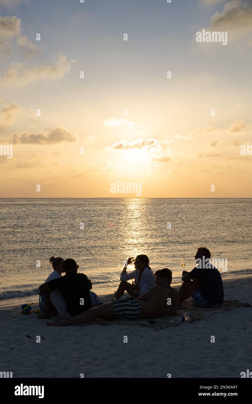 Strandparty - eine Gruppe von Leuten, die im Urlaub am Strand sitzen und bei Sonnenuntergang trinken und den Indischen Ozean überblicken; Rasdhoo-Atoll, die Malediven Stockfoto