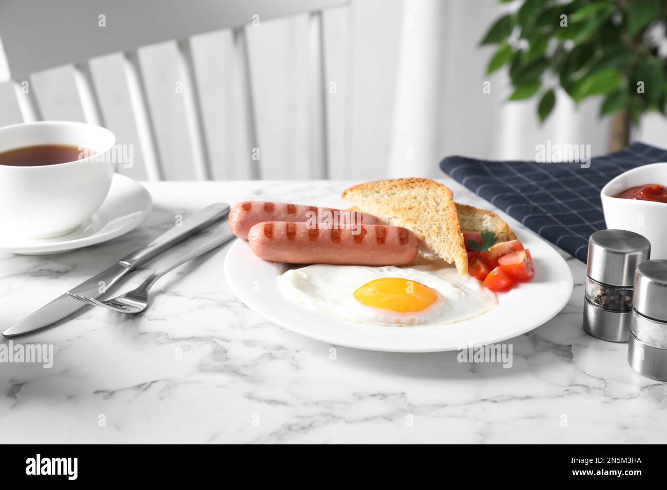 Leckeres Frühstück mit Spiegelei und Würstchen, serviert auf einem weißen Marmortisch im Haus Stockfoto