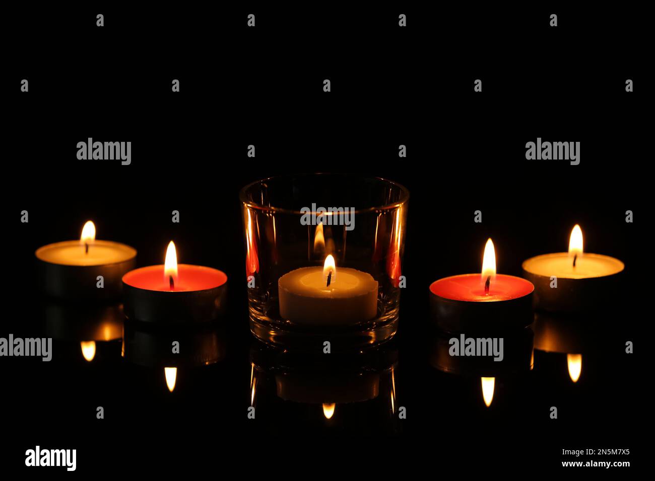 Kleine Wachskerzen brennen in der Dunkelheit. Bestattungssymbol Stockfoto