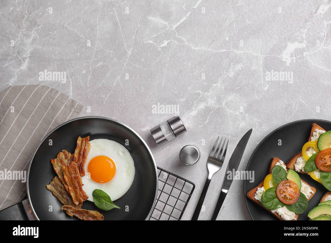 Leckeres Frühstück mit Spiegelei, Speck und Sandwiches, serviert auf einem hellgrauen Marmortisch, flach liegend. Platz für Text Stockfoto