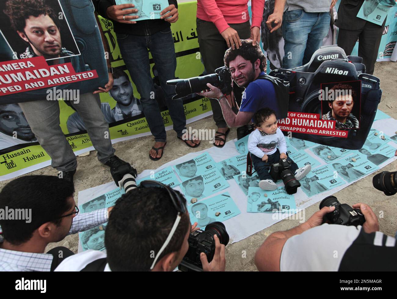 Sayed Redha Humaidan, the 9-month-old son of jailed photographer Sayed Ahmed Humaidan, sits on fliers with images of jailed or killed photographers in front of a cutout of his father during a rally in Sitra, Bahrain, on Friday Jan. 24, 2014. A few thousand people, many waving Bahraini flags, participated in the rally organized by opposition groups demanding democracy in the Gulf island kingdom. (AP Photo/Hasan Jamali) Stockfoto