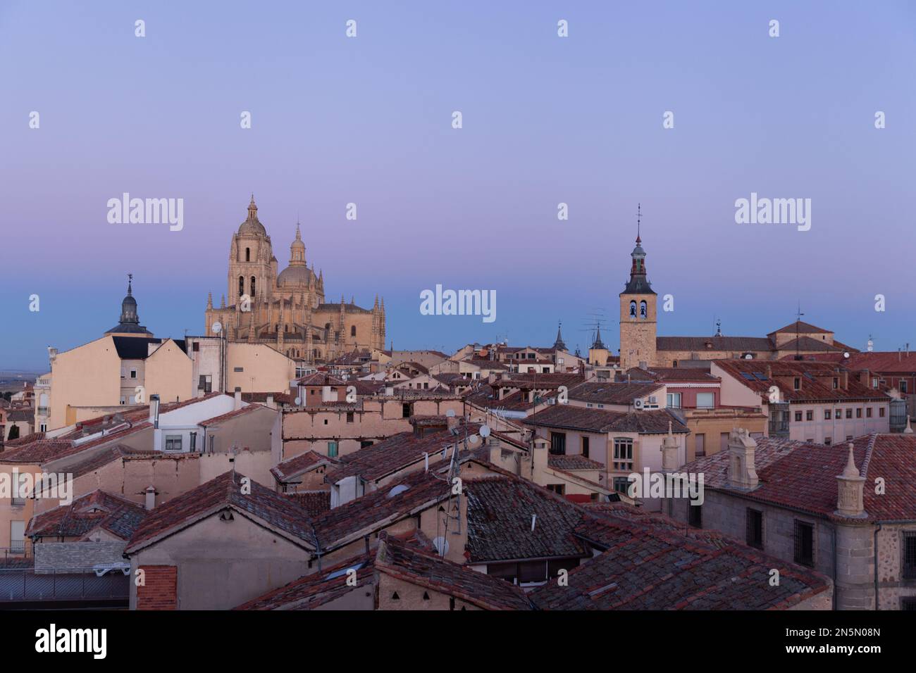 Segovia, Spanien - 4. Januar 2022: Panoramablick auf Segovia mit den Türmen der Kathedrale bei Sonnenuntergang und violettem Himmel im Winter mit dem Guadarrama-Gebirge Stockfoto