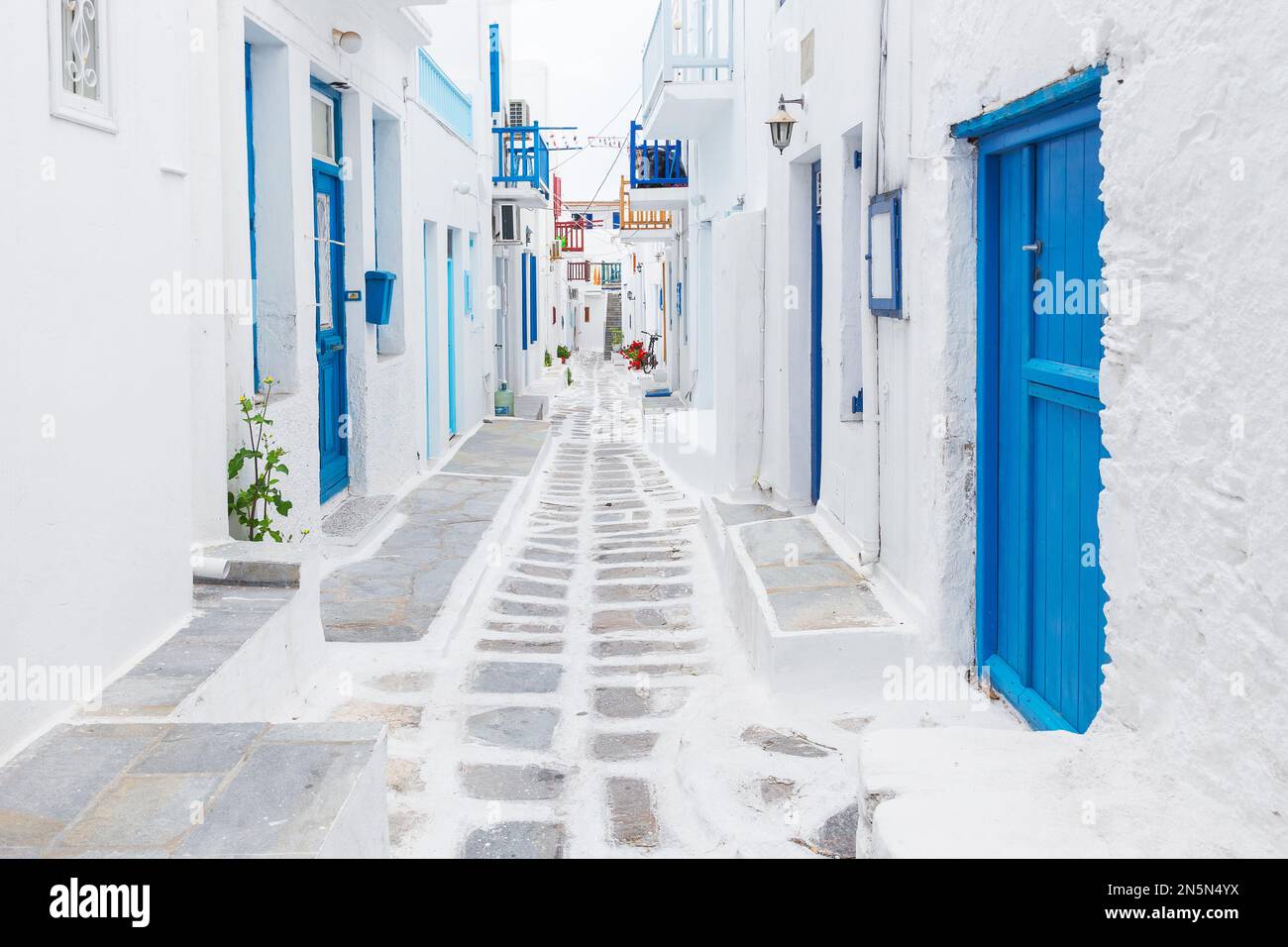 Mykonos, Griechenland: Traditionelle weiß getünchte Straße der Stadt Mykonos mit blauen Fenstern und Türen an einem sonnigen Sommermorgen. Leere Gasse bei Sonnenaufgang Stockfoto