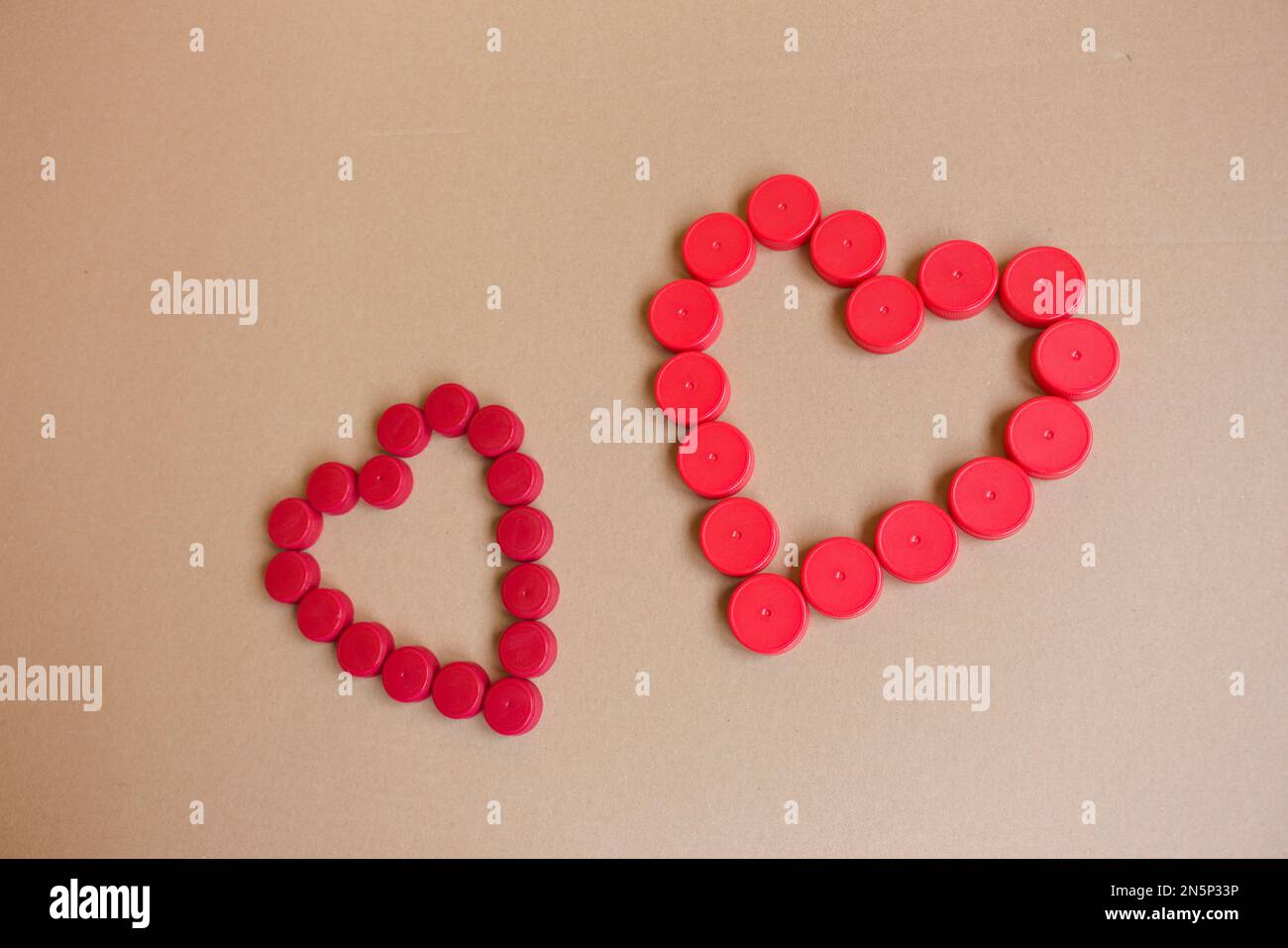 Umweltfreundliches Valentinstagsgeschenk. Zwei Herzen aus Plastikkappen auf braunem Papierhintergrund. Stockfoto