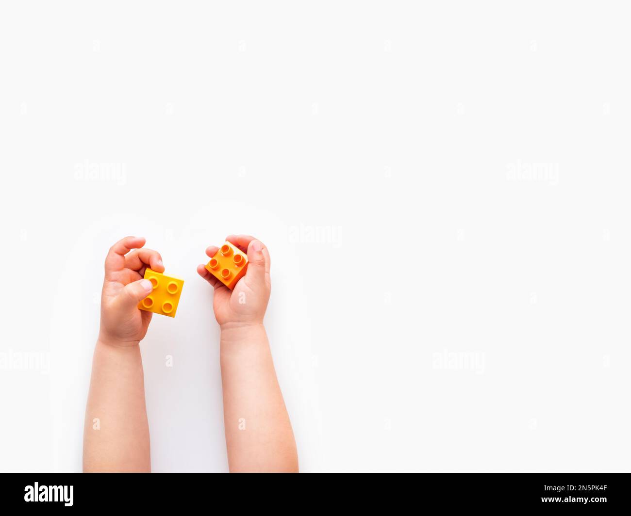 Das Kind beherbergt orangefarbene und blaue Bausteine in der Faust. Kinderhände mit Ziegelspielzeug auf weißem Hintergrund. Pädagogisches Spielzeug, flach liegend, Draufsicht. Stockfoto