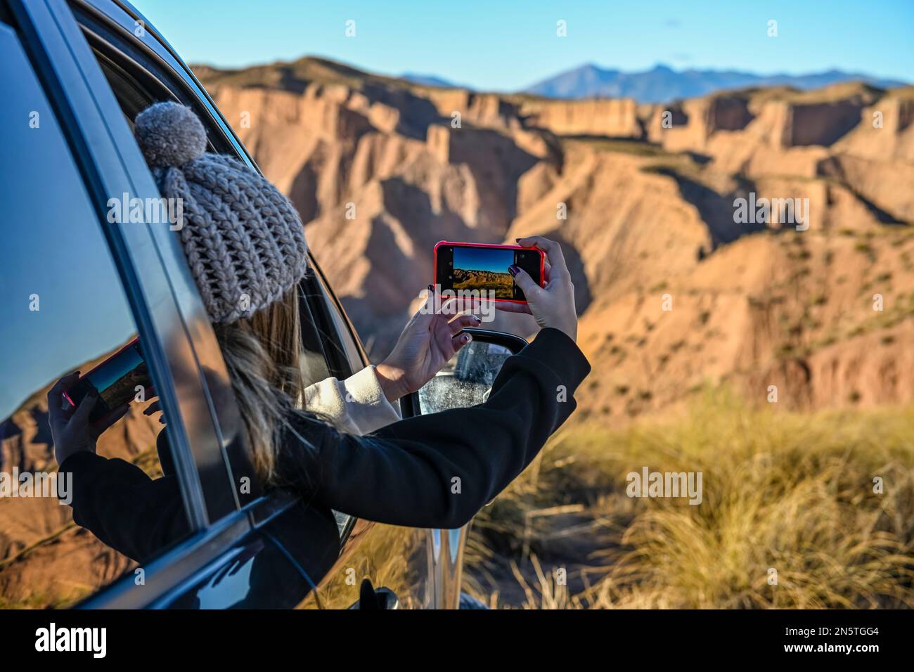 Ein junges Mädchen, das durch ein Autofenster Fotos von der Wüstenlandschaft macht Stockfoto