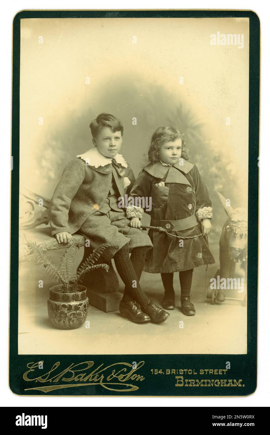 Originale viktorianische Kabinettskarte 2 Arbeiterkinder (wahrscheinlich Jungen in verflixten Socken) in Lord Fauntleroy Outfits, die vielleicht vom Studio geliefert werden. Studio of E S Baker & Son 154 Bristol St., Birmingham, England, Großbritannien 1896 - 1899. Stockfoto
