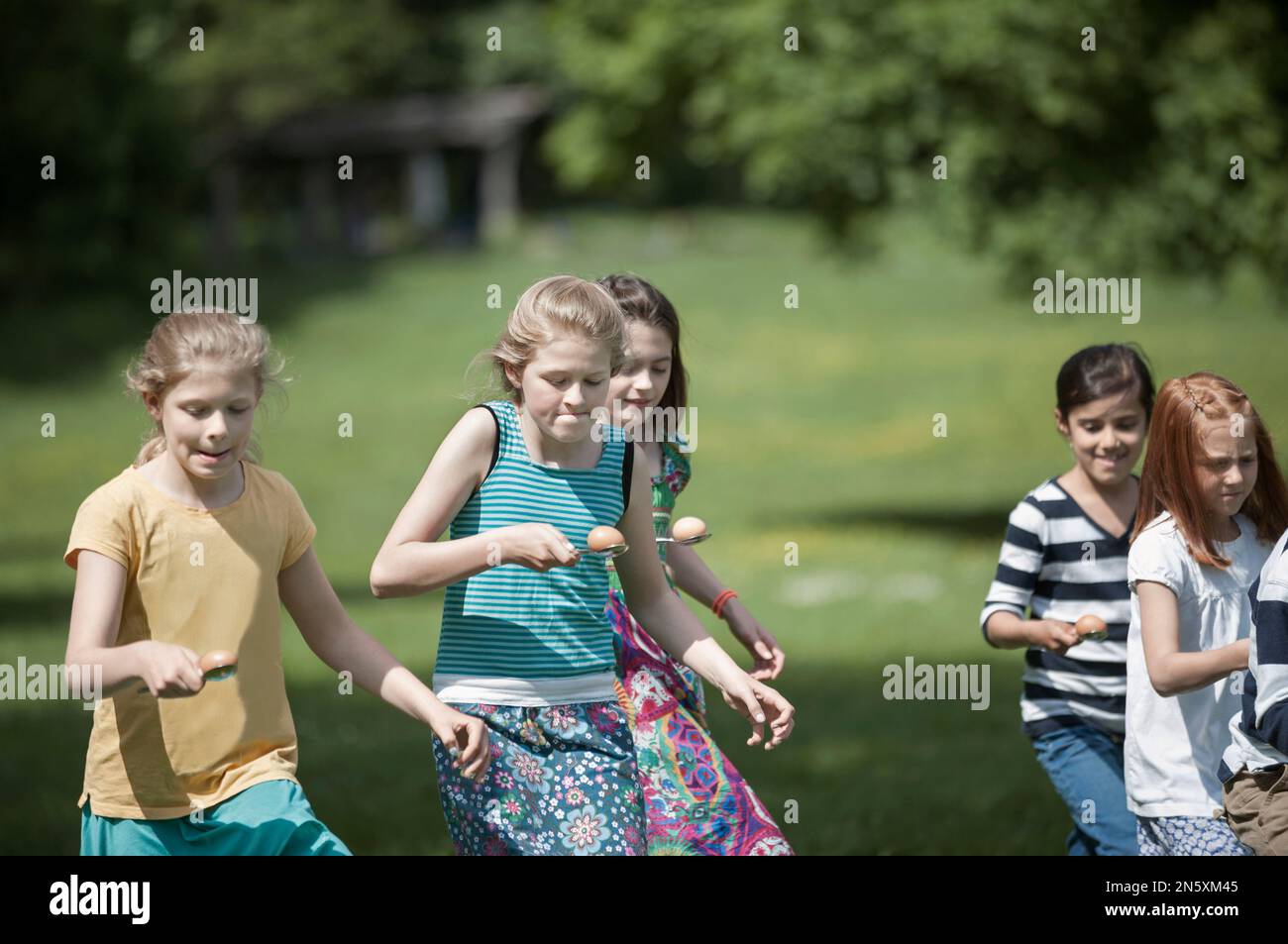 Eine Gruppe von Mädchen, die in einem Ei-Löffel-Rennen in einem Park in München, Bayern, Deutschland, gegeneinander antreten Stockfoto