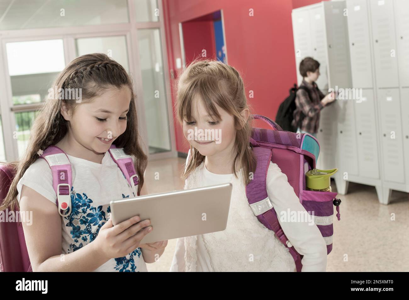 Zwei Schulmädchen, die sich ein digitales Tablet im Korridor in der Nähe von Schließfächern ansehen, Bayern, Deutschland Stockfoto