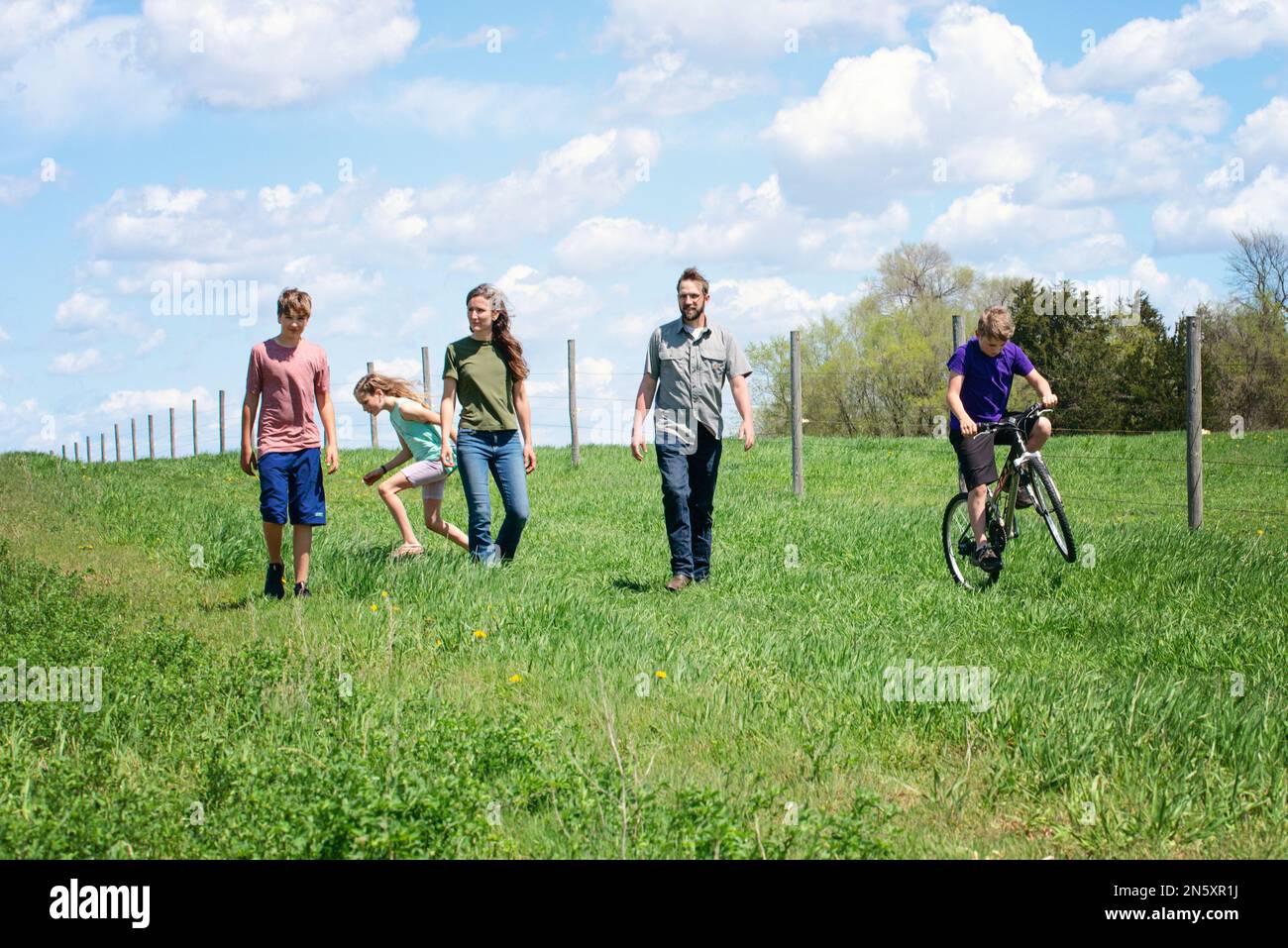 Glückliche fünfköpfige Familie, die an einem Zaun durch das Land läuft. Stockfoto
