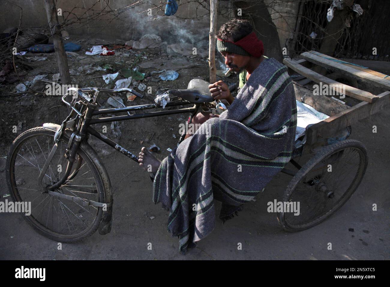 An Indian rickshaw puller wrapped in a blanket, smokes while sitting in his rickshaw in Hyderabad, India, Saturday, Dec. 21, 2013. Though India is famous for its brutally hot summers, temperatures fall sharply for a few weeks in December and January. Poor people, particularly those living on the streets, are the worst affected. (AP Photo/Mahesh Kumar A.) Stockfoto
