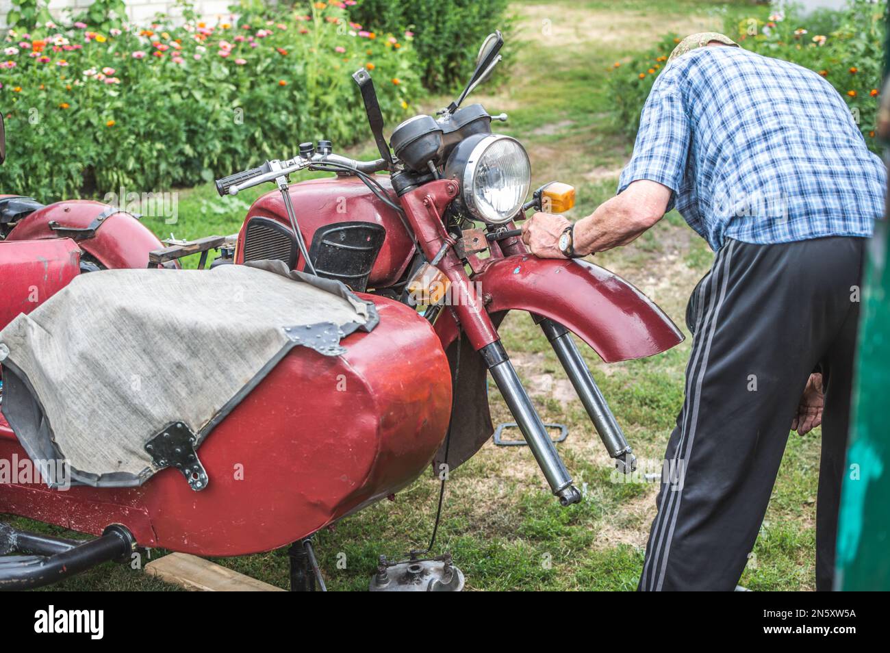 Ein alter Mann repariert ein Retro-Motorrad im Sommerhof Stockfoto