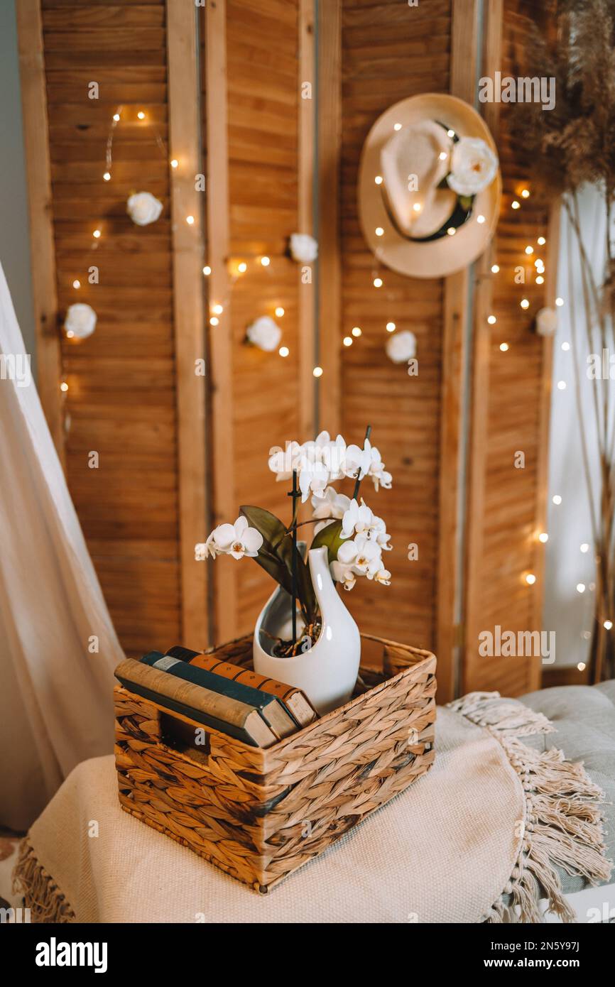 Vintage-Bücher und weiße Orchidee in einem natürlichen Korb, auf einer Bank, gemütlich und weich. Gemütliches Zimmer in Weiß und Beige Stockfoto