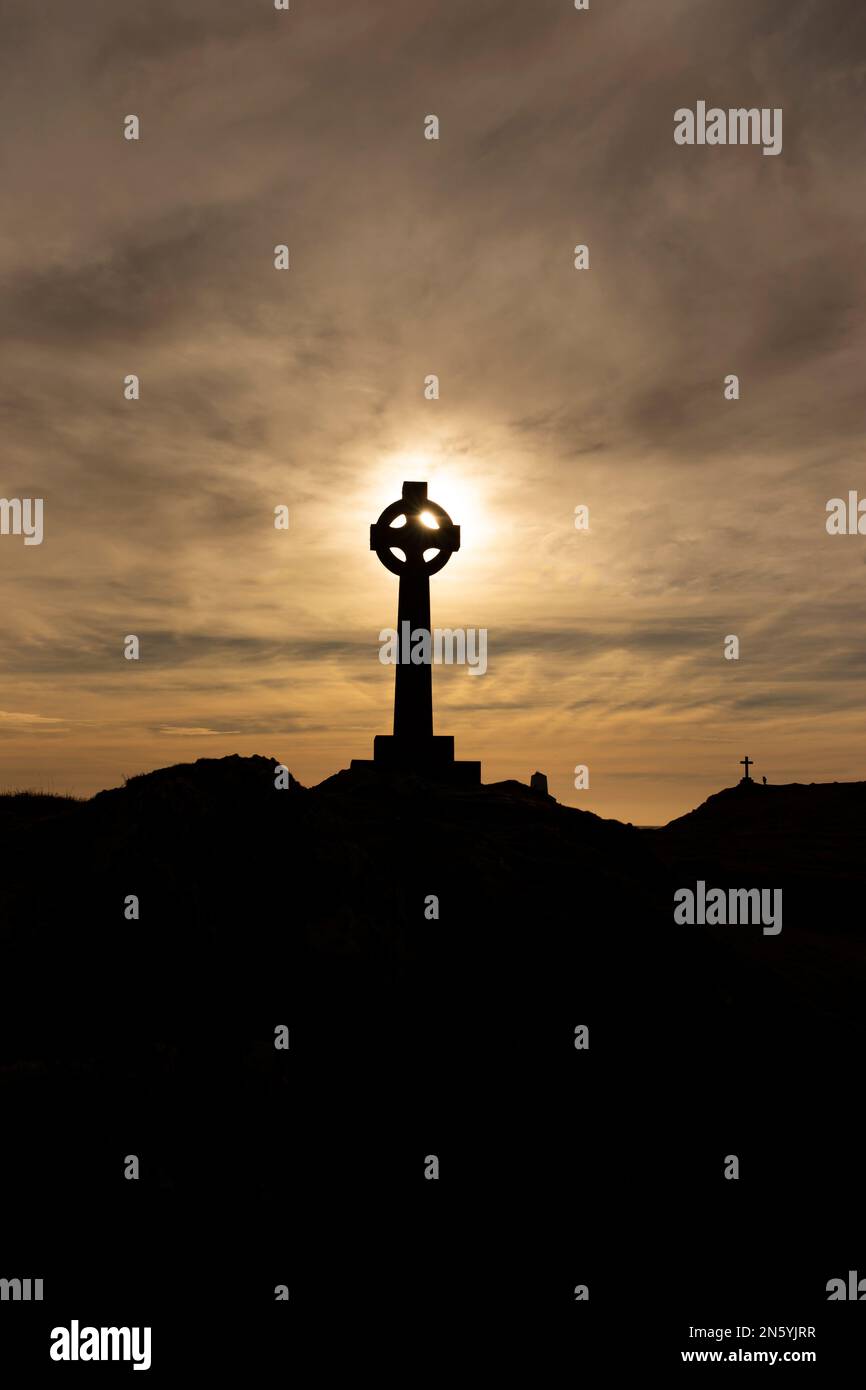 Silhouette eines keltischen Kreuzes mit der Abendsonne direkt dahinter. Mit einem christlichen Kreuz im Hintergrund Stockfoto