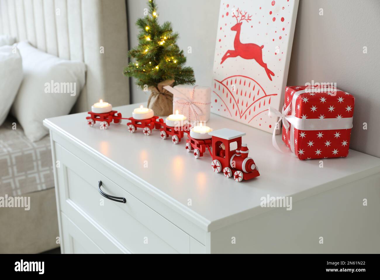 Roter Spielzeugzug als weihnachtlicher Kerzenhalter auf weißer Kommode im Innenbereich Stockfoto