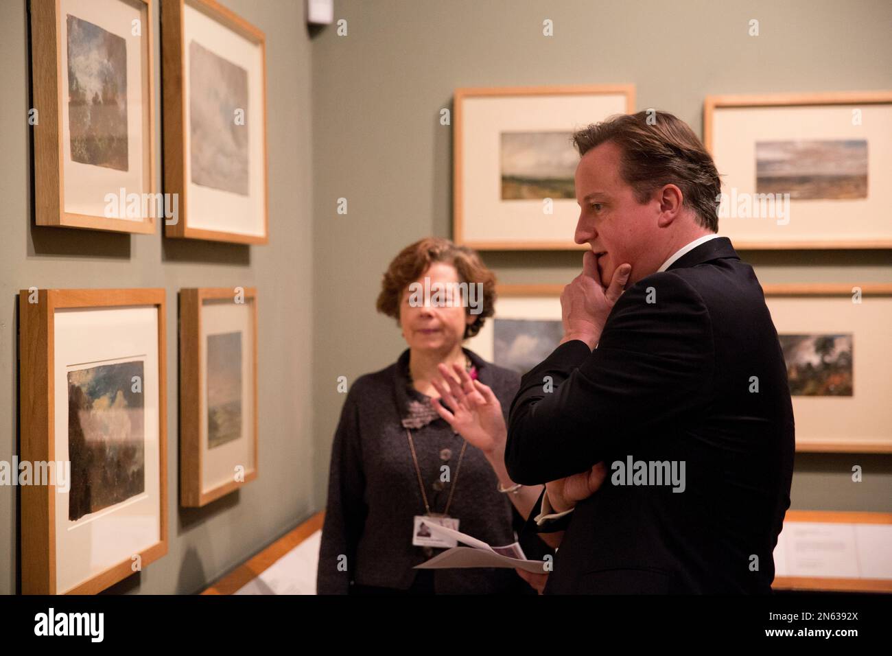 British Prime Minister David Cameron, right, is shown the newly discovered previously unknown oil sketch painting by John Constable entitled "Landscape with a Kiln" from 1821 or 1822 by Head Painting Conservator Nicola Costaras, below left, as an additional part of his visit to the "Masterpieces of Chinese Painting: 700-1900" at the Victoria & Albert Museum in London, Thursday, Nov. 28, 2013. The museum said it was discovered when conservators attempted to remove the lining on the back of "Branch Hill Pond: Hampstead", another work by the English romantic painter known for his landscapes, whil Stockfoto