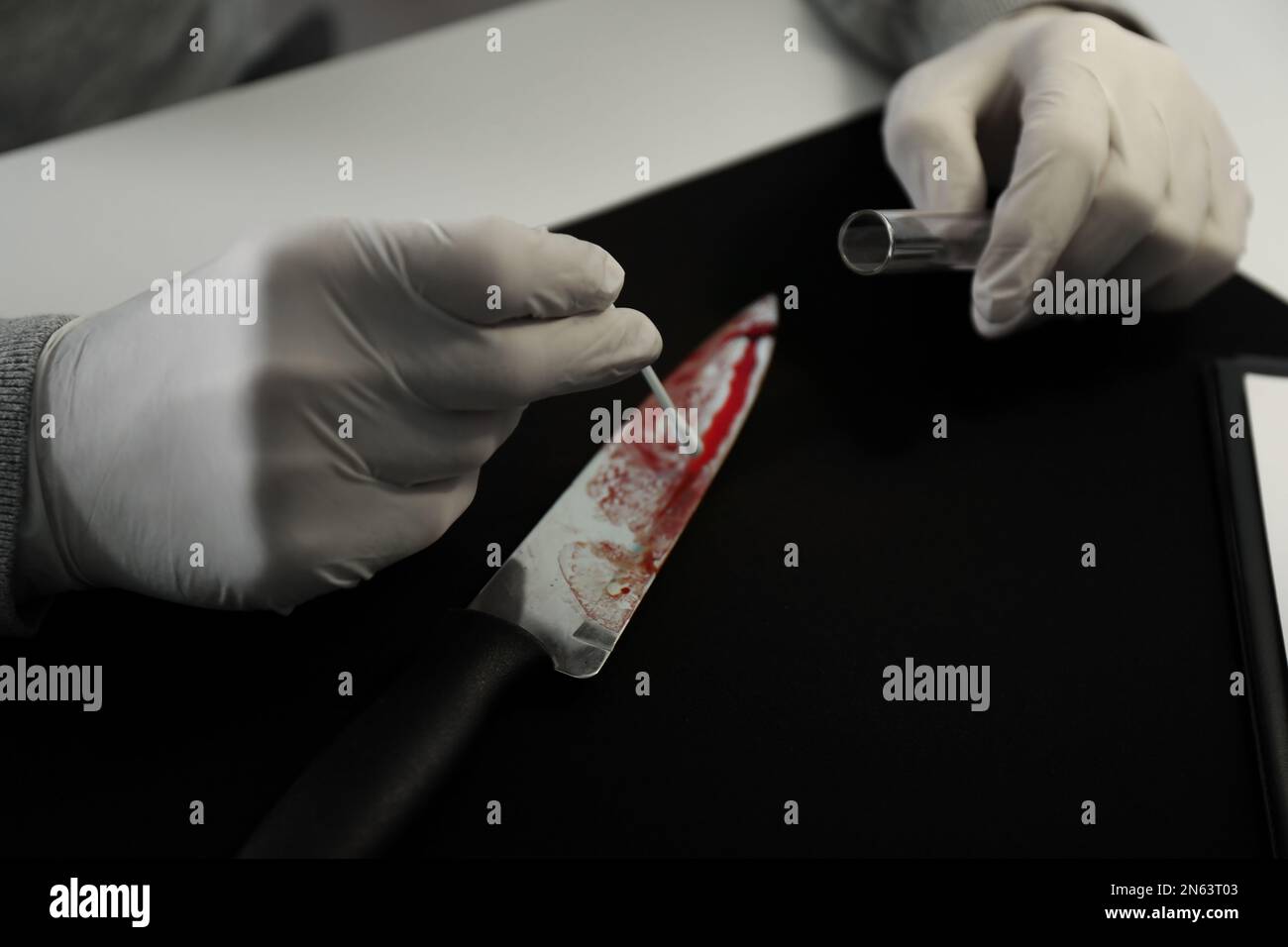 Detective nimmt DNA-Probe von Blut vom Messer am Tisch, Nahaufnahme Stockfoto