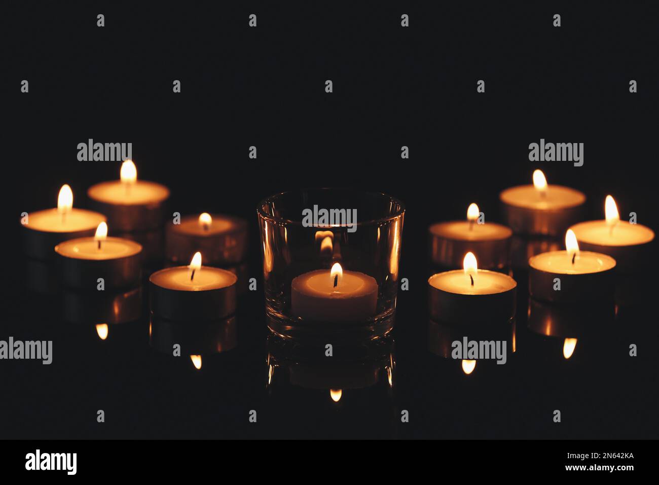 Kleine Wachskerzen brennen in der Dunkelheit. Bestattungssymbol Stockfoto