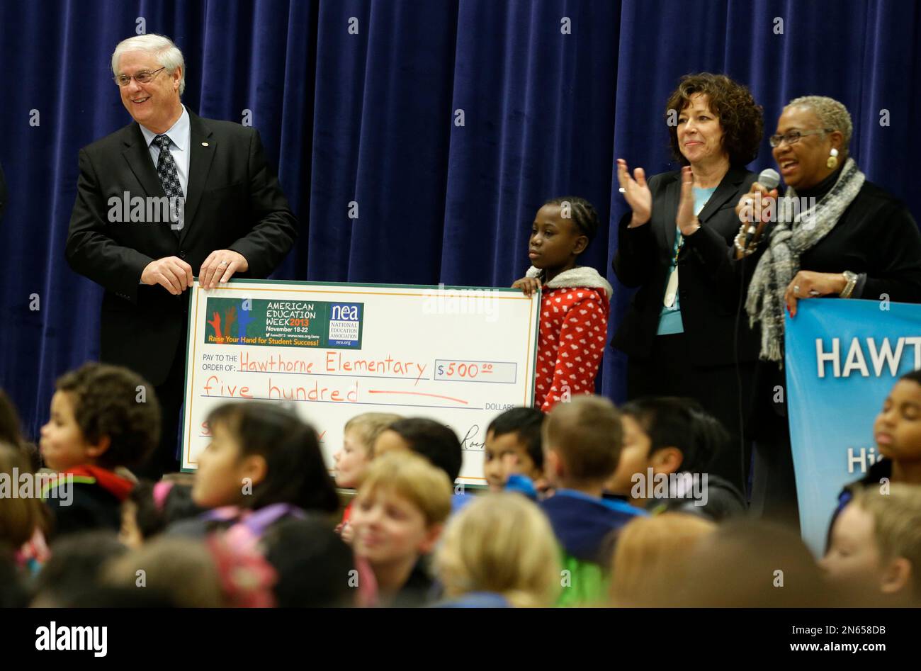 National Education Association president Dennis Van Roekel, left, stands with Hawthorne Elementary president Quison Ash, 10, second from left, Kim Mead, second from right, president of the Washington Education Association, and Sandra Scott, right, president of Hawthorne Elementary School, Monday, Nov. 18, 2013 during a visit to the school in Seattle. Van Roekel presented the school with a check for $500 to purchase items for the school library. (AP Photo/Ted S. Warren) Stockfoto