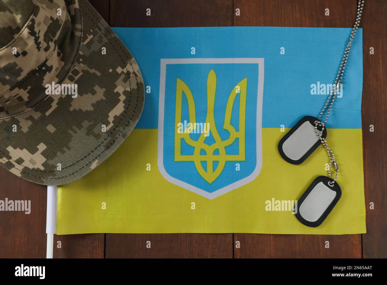 MYKOLAIV, UKRAINE - 26. SEPTEMBER 2020: Militärmütze, Kennzeichnungen und ukrainische Flagge auf Holztisch, flach liegend Stockfoto