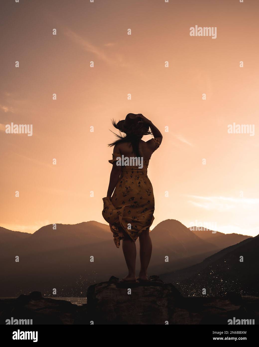 Silhouette eines Mädchens im Wind am Meer mit Berglichtern Stockfoto