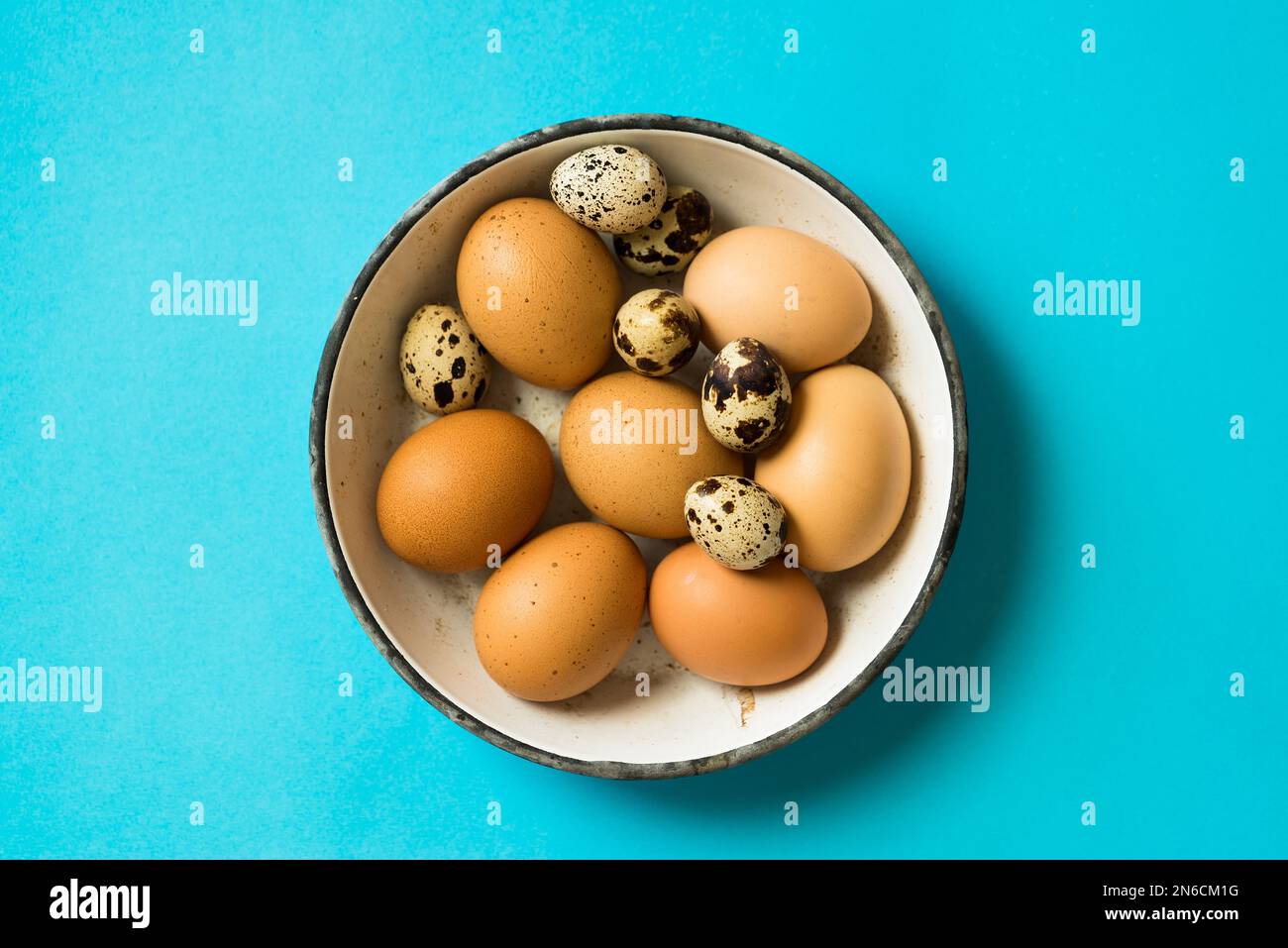 Eier in einer Schmelzschüssel auf neonblauem Hintergrund. Tischplatte direkt über der Aufnahme. Stockfoto