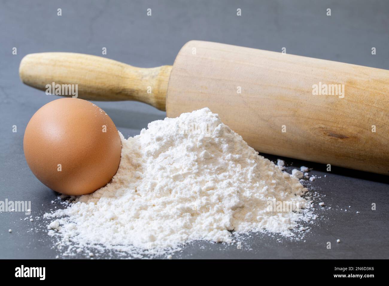 Haufen Allzweckmehl und Ei für die Herstellung von hausgemachtem Brot auf dunklem Hintergrund. Stockfoto