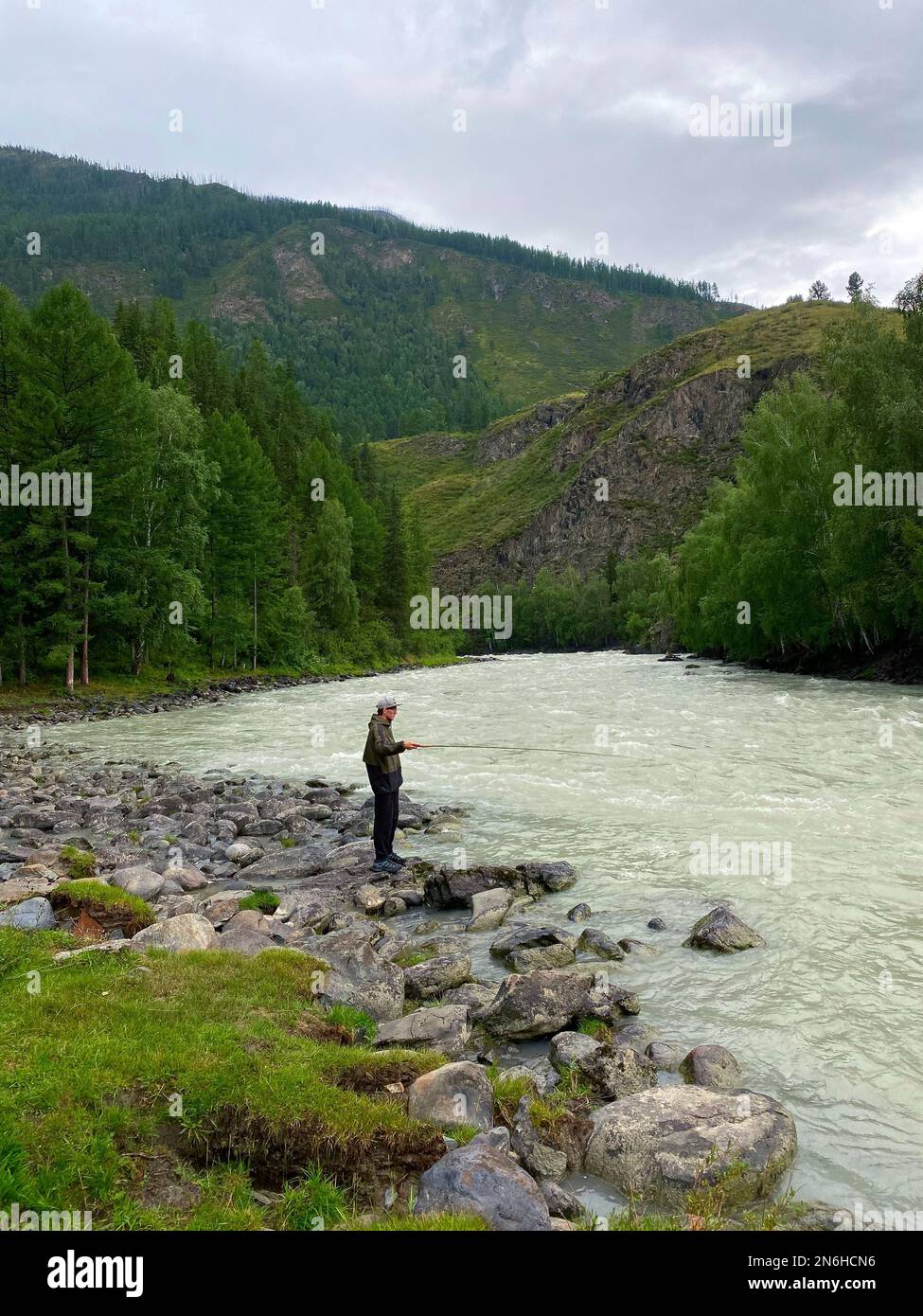 Ein Fischer steht am Ufer eines Bergflusses mit einer Angelrute. Stockfoto