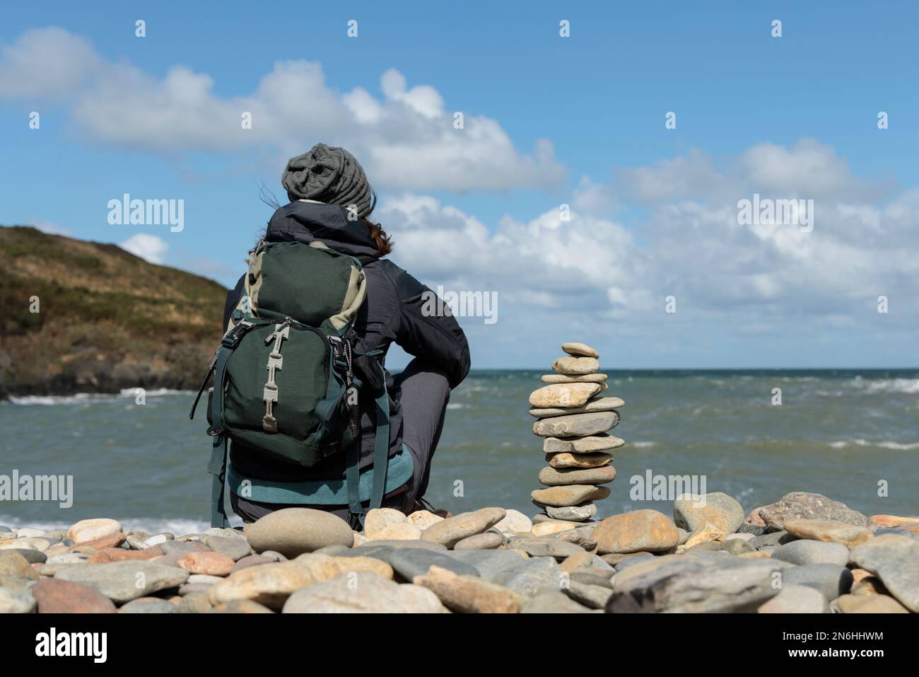 Eine Frau, die allein sitzt und auf das Meer an einem Kieselstrand in Wales schaut. Stockfoto