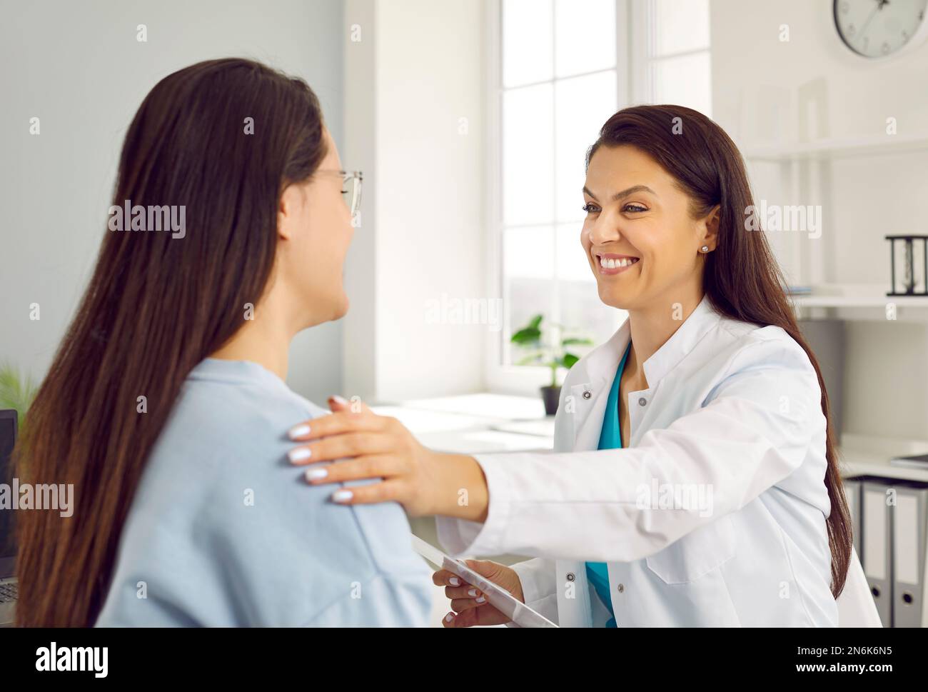 Eine freundliche, lächelnde Ärztin, die die Schulter der Frau hält und ihr positive Nachrichten über ihre Gesundheit mitteilt. Stockfoto
