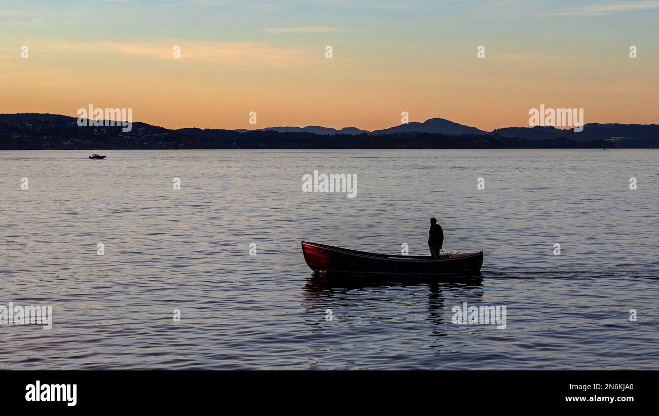 Ein Mann in einem kleinen Boot, in Byfjorden, bei Sonnenuntergang. Außerhalb des Hafens Bergen, Norwegen. Stockfoto