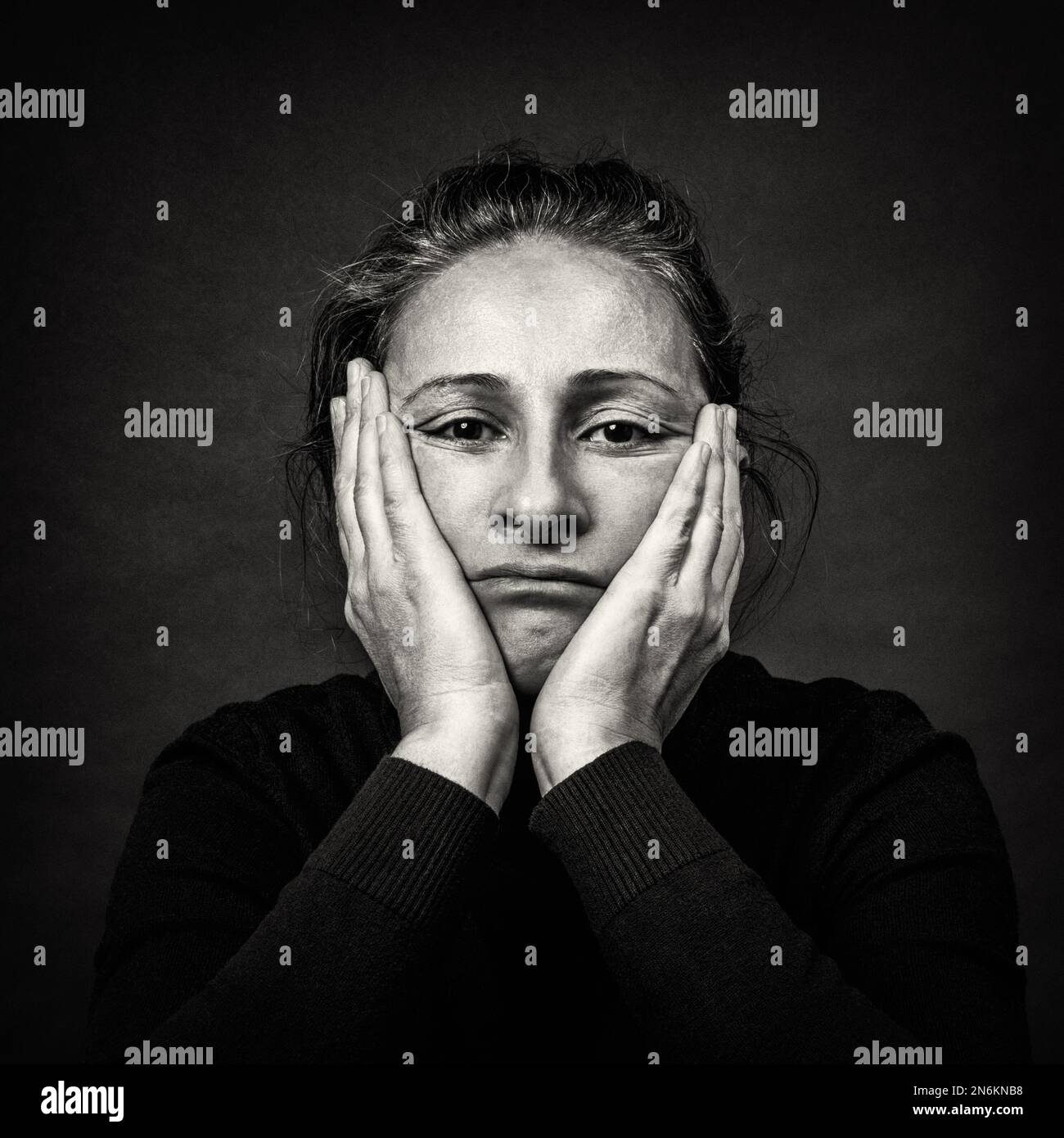 Begriffliches dunkles Porträt einer alten traurigen Frau mit Händen über dem Kopf in hässlicher Grimasse. Schwarzweiß-Filmkörnung. Stockfoto