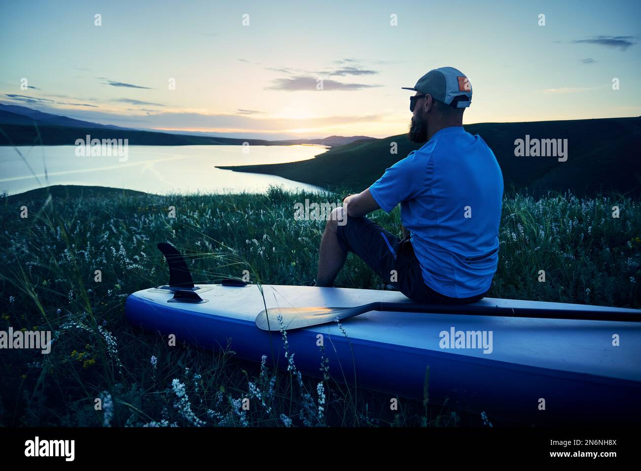 Porträt eines bärtigen Mannes in Silhouette mit SUP-Paddel in der Nähe des Sees bei Sonnenuntergang in Kasachstan. Stand Up Paddle Boarding Outdoor aktiv Erholung i Stockfoto