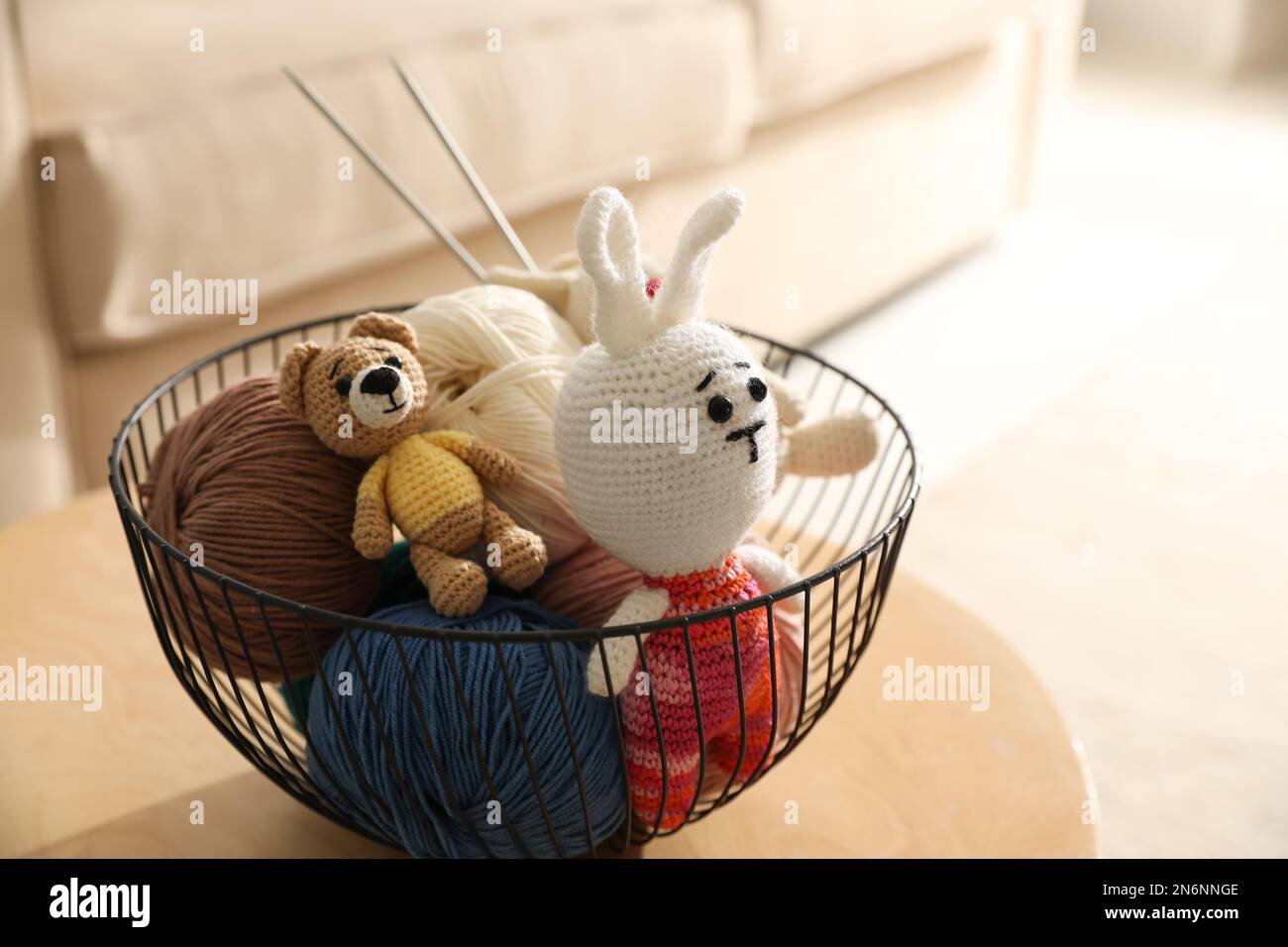 Korb mit Farbfäden und gestricktem Spielzeug auf dem Tisch im Innenbereich. Handwerk als Hobby Stockfoto