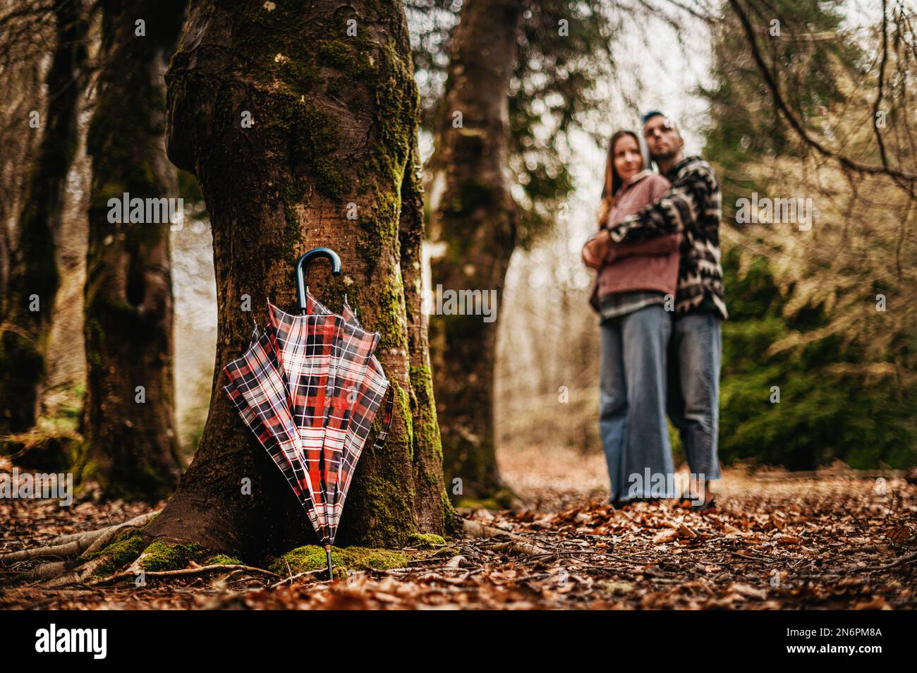 Ein Paar steht neben einem Baum mit einem gemusterten Schirm im Vordergrund Stockfoto