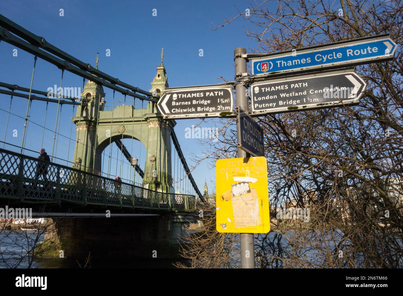 Beschilderung zum Thames Cycle Path und eine noch immer fest geschlossene Hammersmith Bridge, die repariert wird und auf die Planungsgenehmigung für eine neue Straßenoberfläche wartet Stockfoto