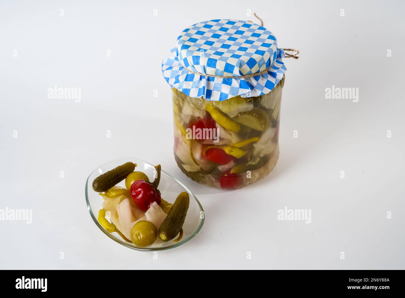 Gemischte Gewürzgurken, Sauerkraut, Pfeffer, Tomaten- und Gurkenpickles in Glasgefäß und Teller, isoliert auf weißem Hintergrund. Stockfoto