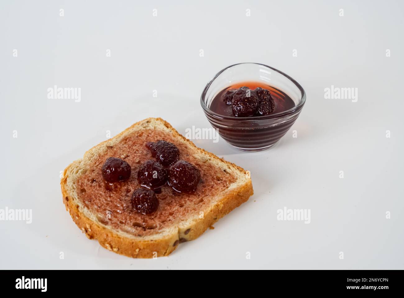 Hausgemachte Erdbeermarmelade, kleine Schüssel und eine Scheibe Brot mit isolierter Marmelade auf weißem Hintergrund. Stockfoto