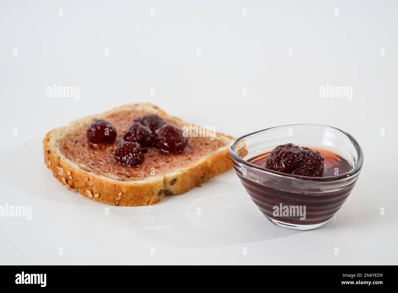 Hausgemachte Erdbeermarmelade, kleine Schüssel und eine Scheibe Brot mit isolierter Marmelade auf weißem Hintergrund. Stockfoto