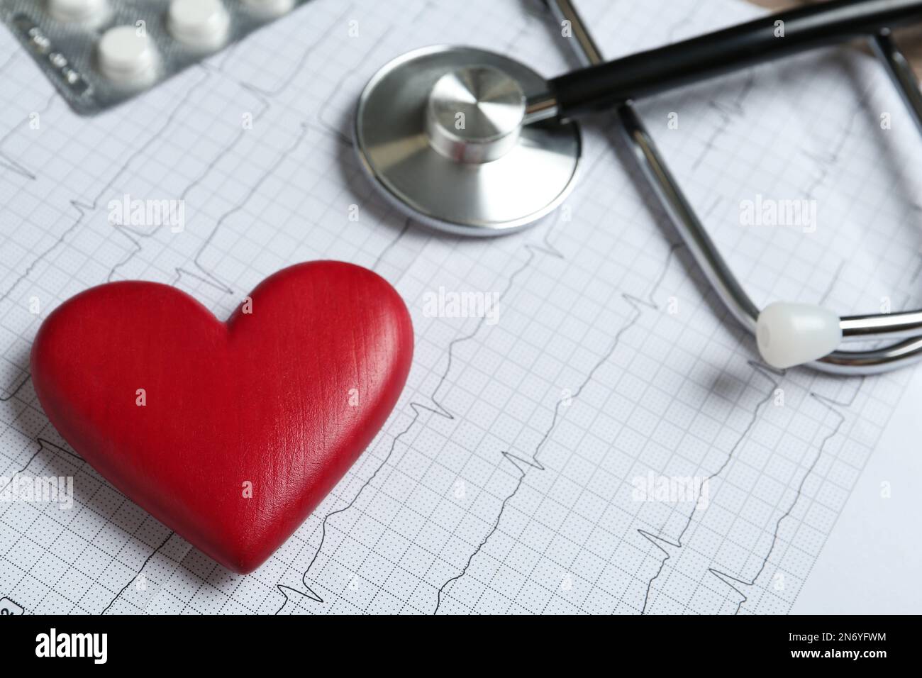 Rotes dekoratives Herz, Pillen und Stethoskop im Kardiogramm, Nahaufnahme Stockfoto