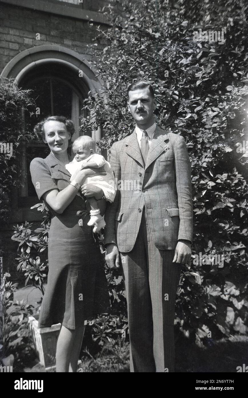 1940er Jahre, historisch, ein gut gekleidetes, aristokratisches englisches Paar, das draußen für ein Foto steht, die Dame, die ihr Baby hält, England, Großbritannien. Gentlemn trägt eine karierte Jacke, Krawatte und Streifenmuster. Stockfoto