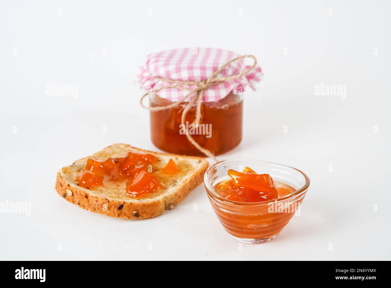 Hausgemachte Aprikosenmarmelade, Glas, kleine Schüssel und eine Scheibe Brot mit isolierter Marmelade auf weißem Hintergrund. Stockfoto