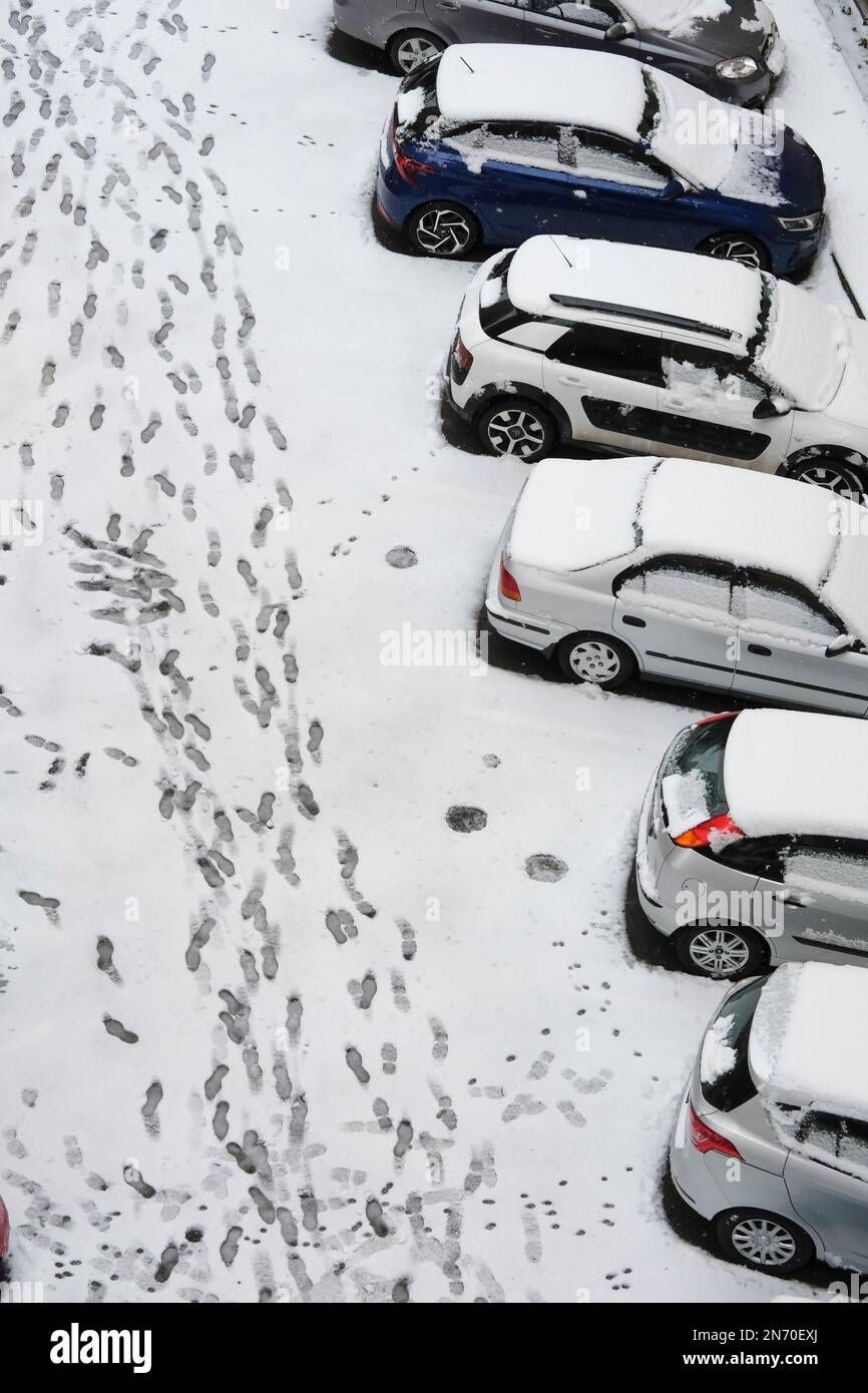 Autos und Asphaltboden sind mit Schnee bedeckt. Es gibt viele Fußspuren auf dem Schnee. Stockfoto