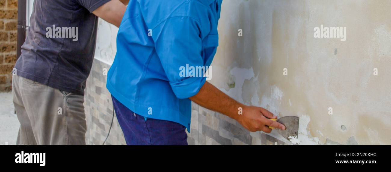 Bild von zwei männlichen Bauarbeitern, die eine Schimmelwand schleifen und reinigen. Problem mit steigender Feuchtigkeit. Stockfoto