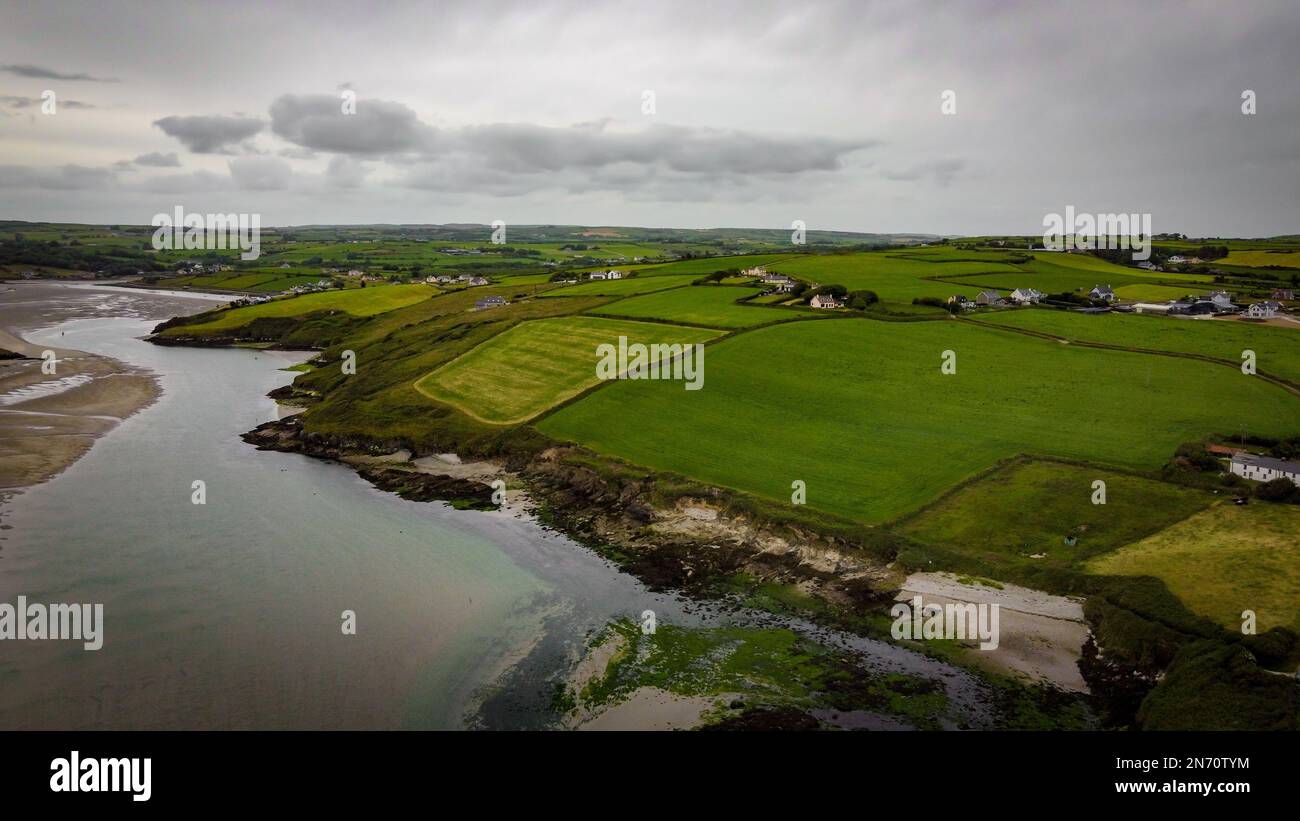 Grüne Felder auf den irischen Hügeln, Draufsicht. Die Landschaft Irlands an einem bewölkten Tag. Die Küste der Clonakilty Bay bei Ebbe. Grünes Grasfeld ununde Stockfoto