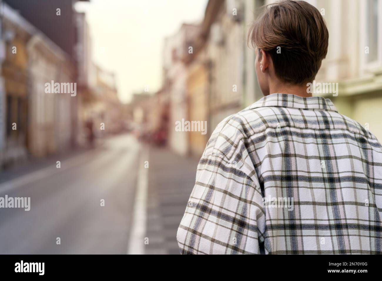 Eine Frau mit kurzen Haaren im karierten Hemd, die in der Stadt die Straße entlang läuft. Stockfoto