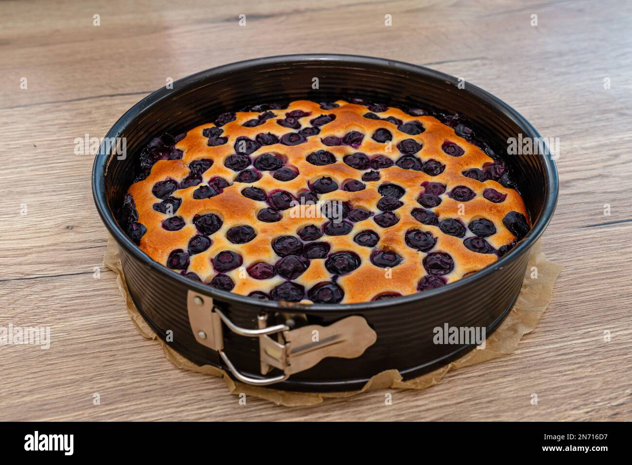 Gebackener Kuchen in runder Form mit Heidelbeere, der auf einem Holztisch liegt. Stockfoto